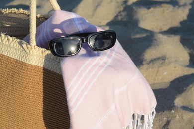 Photo of Stylish wicker bag, sunglasses and blanket on sand, closeup