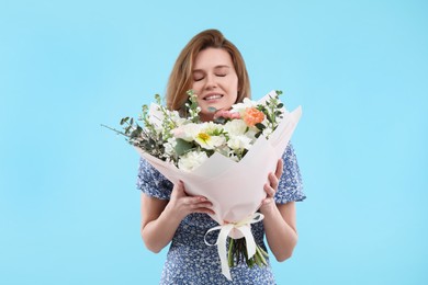 Happy woman with bouquet of beautiful flowers on light blue background
