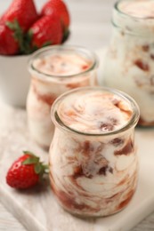 Photo of Tasty yoghurt with jam and strawberries on white marble board, closeup