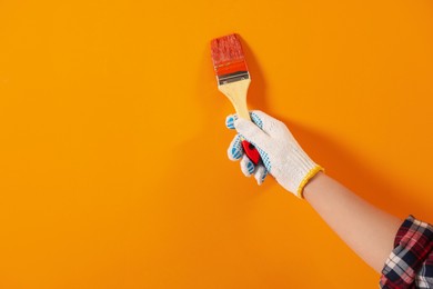 Designer painting orange wall with brush, closeup. Space for text