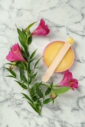 Spatula with wax and flowers on white marble table, flat lay