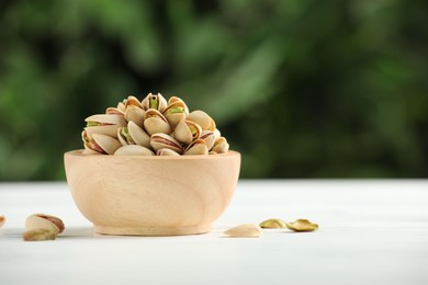 Photo of Tasty pistachios in bowl on white wooden table against blurred background, closeup. Space for text