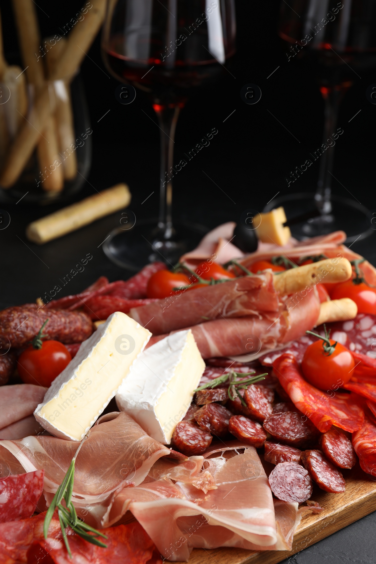 Photo of Tasty prosciutto with other delicacies served on black table