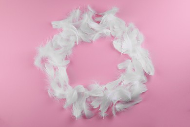 Frame made of fluffy feathers on pink background, flat lay
