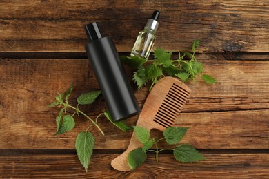 Photo of Stinging nettle extract, cosmetic product and comb on wooden background, flat lay. Natural hair care