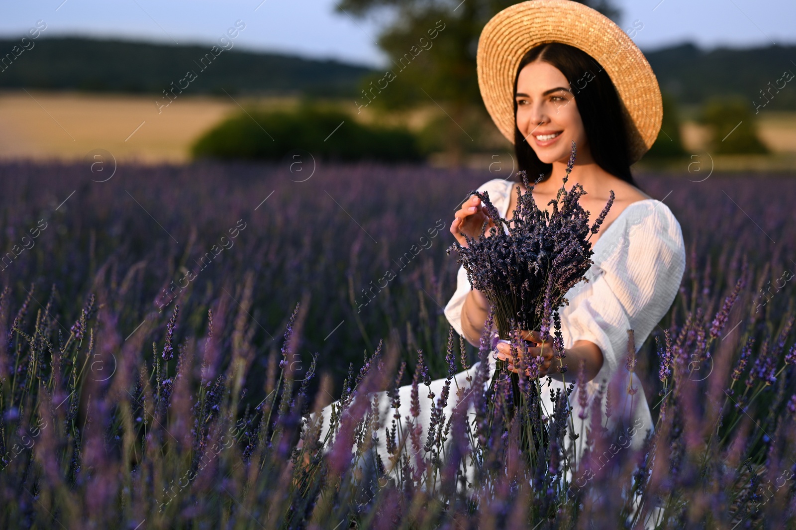 Photo of Beautiful young woman with bouquet sitting in lavender field