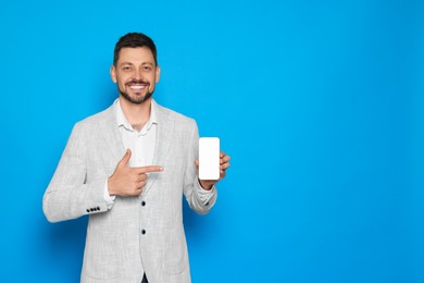 Happy man pointing at smartphone on light blue background. Space for text