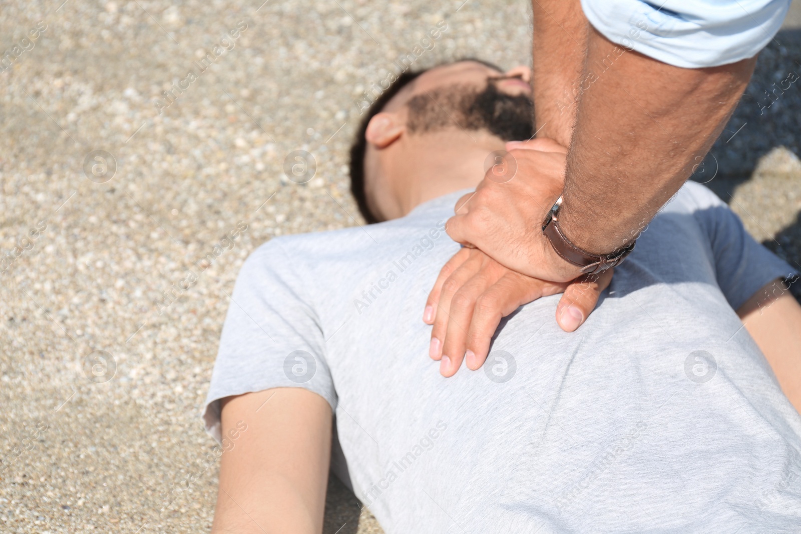 Photo of Passerby performing CPR on unconscious young man outdoors, closeup. First aid