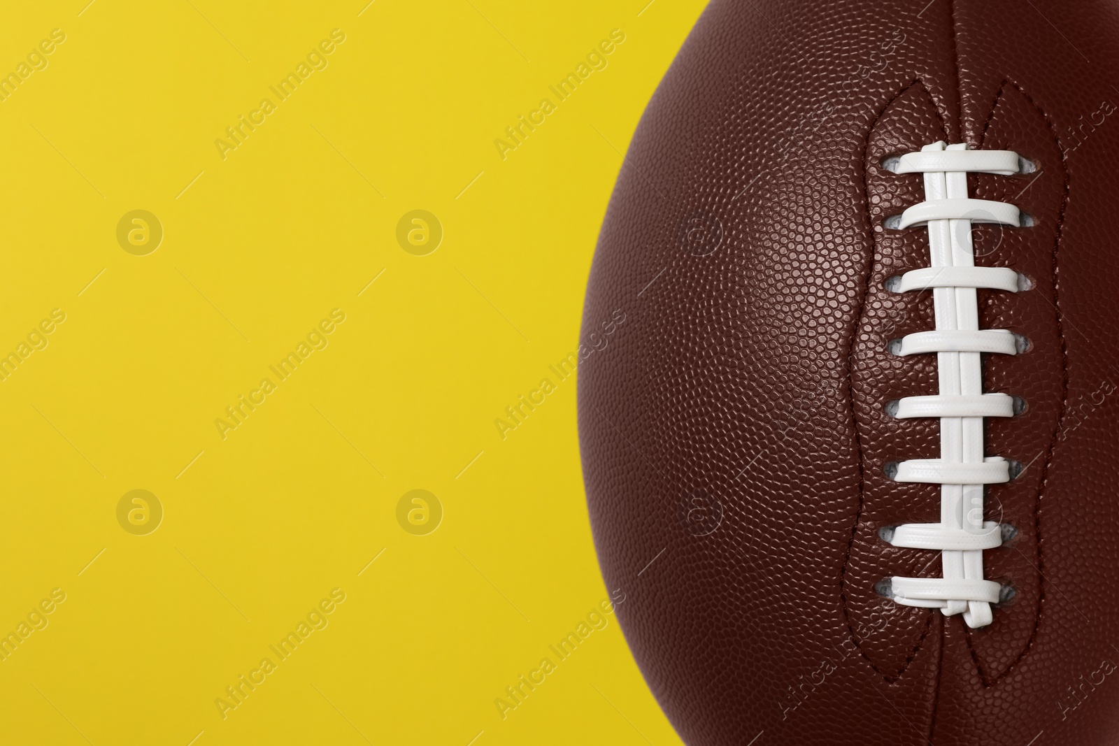 Photo of American football ball on yellow background, top view. Space for text