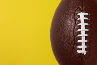 Photo of American football ball on yellow background, top view. Space for text