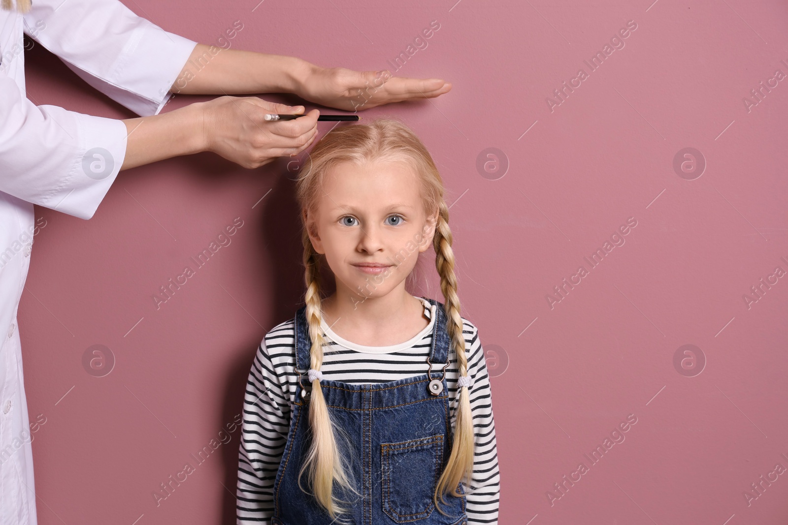 Photo of Doctor measuring little girl's height on color background