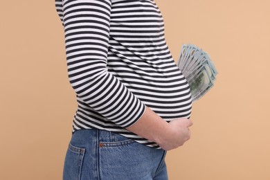 Photo of Surrogate mother. Pregnant woman with dollar banknotes on beige background, closeup