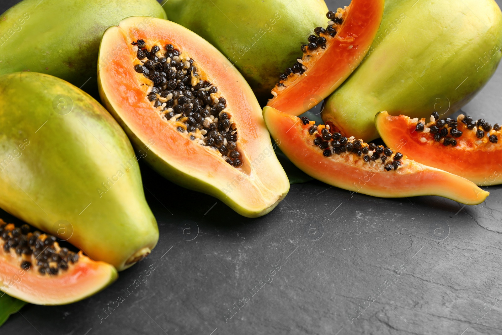 Photo of Cut and whole fresh ripe papaya fruits on black table