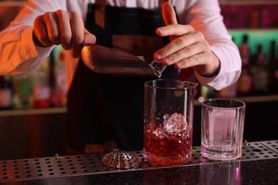 Alcoholic cocktail making. Bartender adding ice cubes into mixing glass at counter in bar, closeup