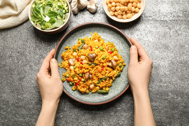 Photo of Woman with plate of delicious rice pilaf at grey table, top view