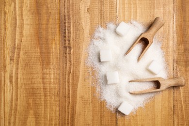 Photo of White sugar with scoops on wooden table, flat lay. Space for text