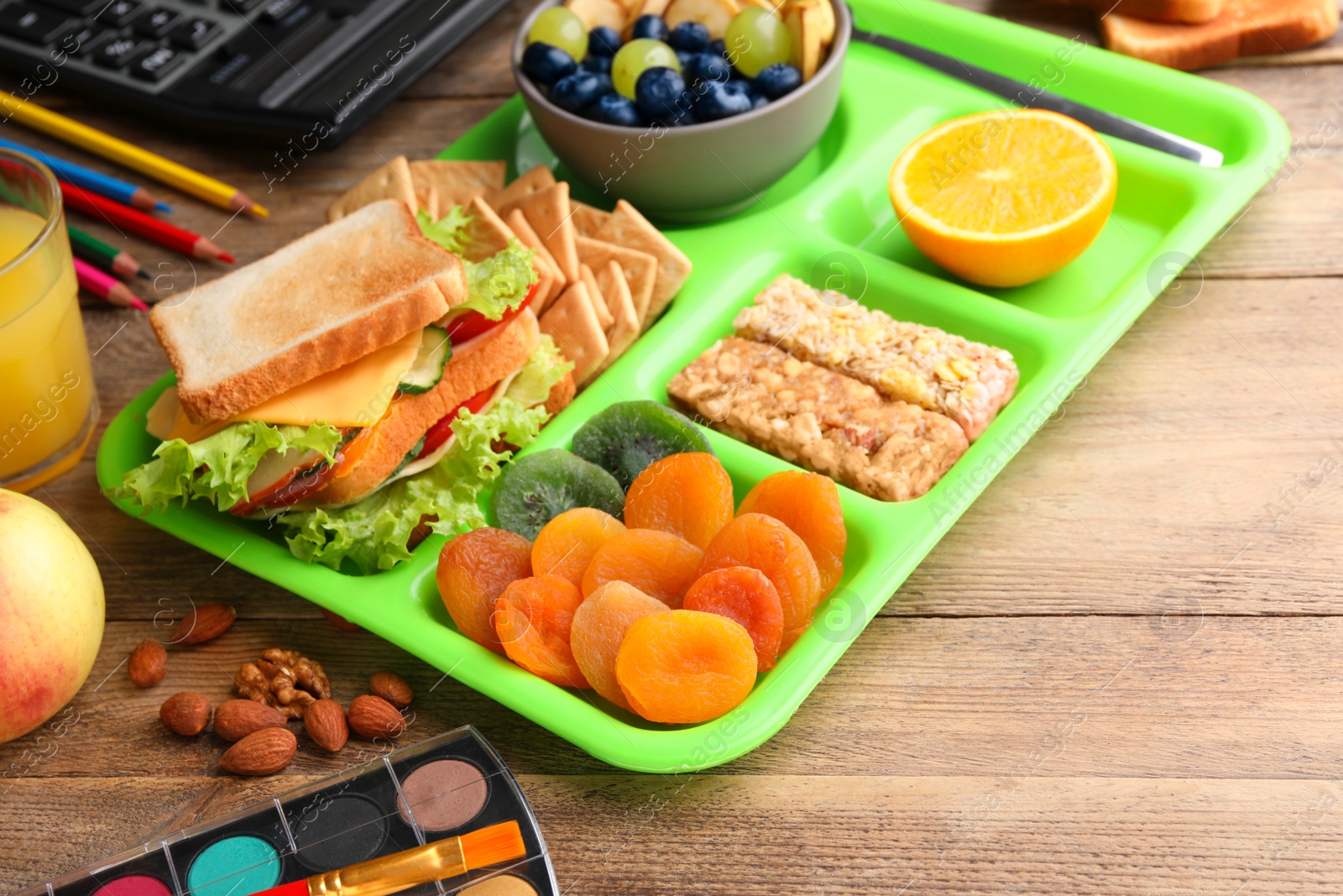 Photo of Serving tray of healthy food and stationery on wooden table. School lunch