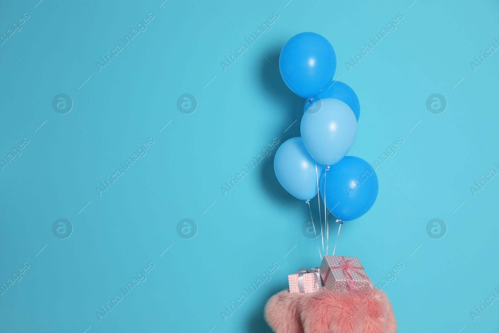 Photo of Bunch of bright balloons and gifts on table against color wall, space for text