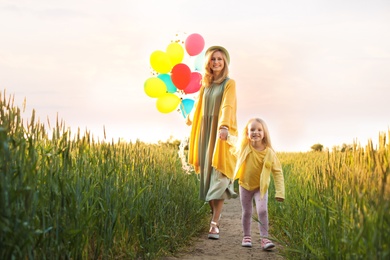 Photo of Young woman and her daughter with colorful balloons outdoors on sunny day