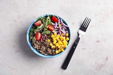 Photo of Healthy quinoa salad with vegetables in bowl and fork on color background, top view