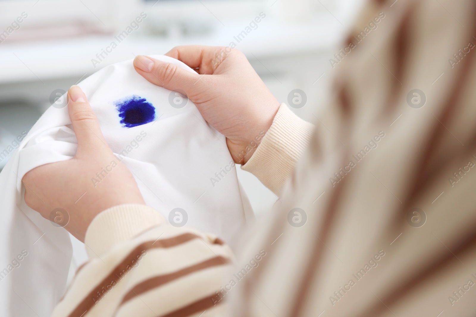 Photo of Woman holding white shirt with blue ink stain on blurred background, closeup