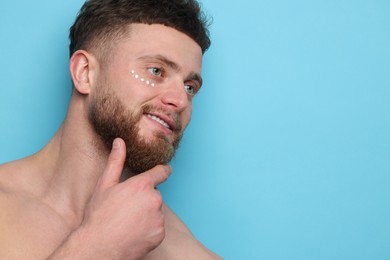 Photo of Handsome man with moisturizing cream on his face against light blue background, space for text