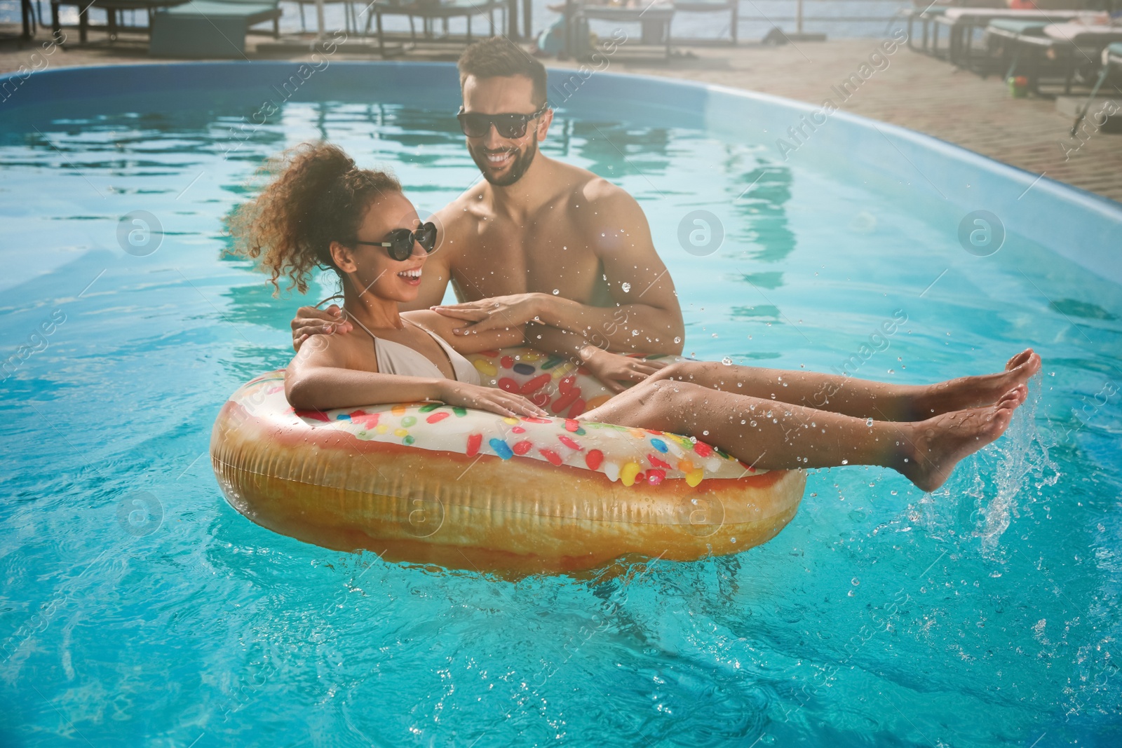 Photo of Happy couple with inflatable ring in outdoor swimming pool on sunny summer day