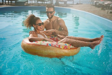 Photo of Happy couple with inflatable ring in outdoor swimming pool on sunny summer day