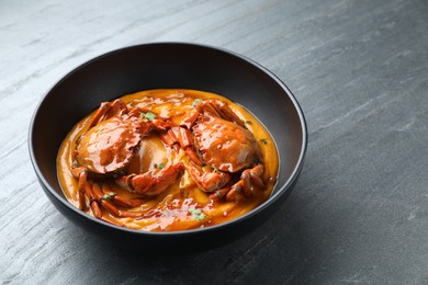 Photo of Delicious boiled crabs with sauce in bowl on grey textured table, space for text