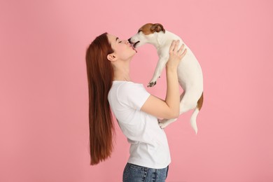 Photo of Woman kissing her cute Jack Russell Terrier dog on pink background