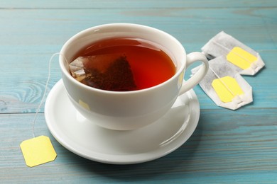 Photo of Tea bags and cup of aromatic drink on light blue wooden table, closeup