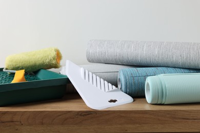 Different wallpaper rolls, plastic spatula and roller on wooden table