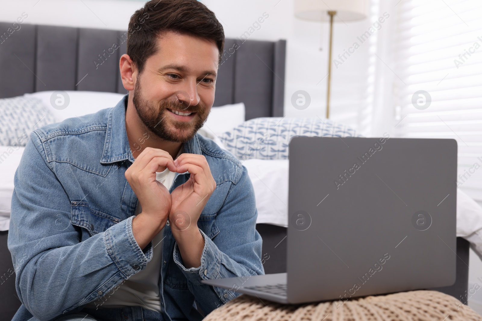 Photo of Happy man making heart with hands during video chat via laptop at home. Long-distance relationship