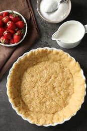 Photo of Making shortcrust pastry. Raw dough in baking dish, strawberries, sugar and milk on grey table, top view