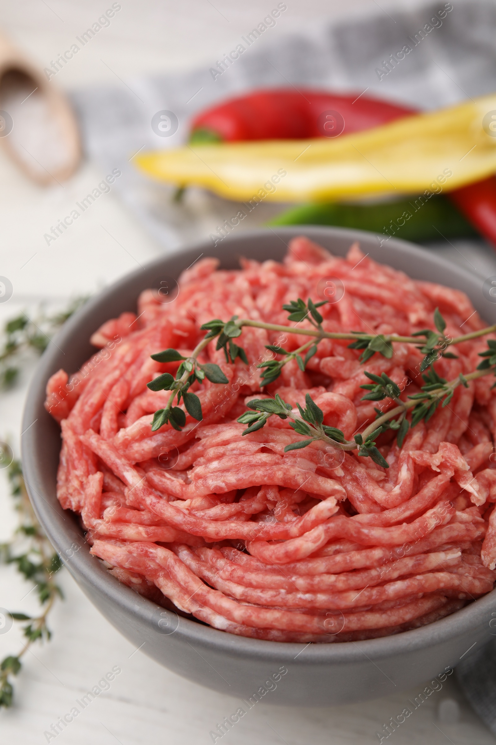 Photo of Fresh raw ground meat and thyme in bowl on white table, closeup