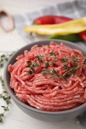 Fresh raw ground meat and thyme in bowl on white table, closeup