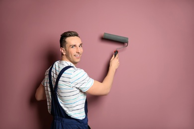 Young male decorator with paint roller near color wall