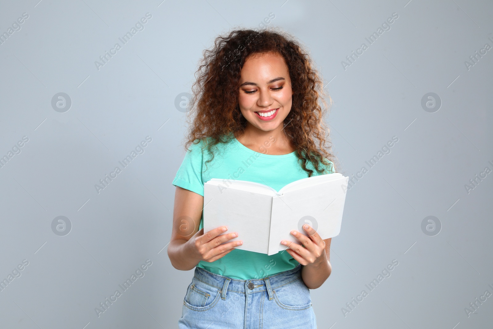 Photo of Beautiful African-American young woman reading book on light background