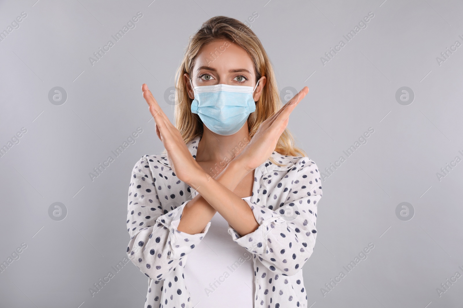 Photo of Woman in protective face mask showing stop gesture on grey background. Prevent spreading of coronavirus