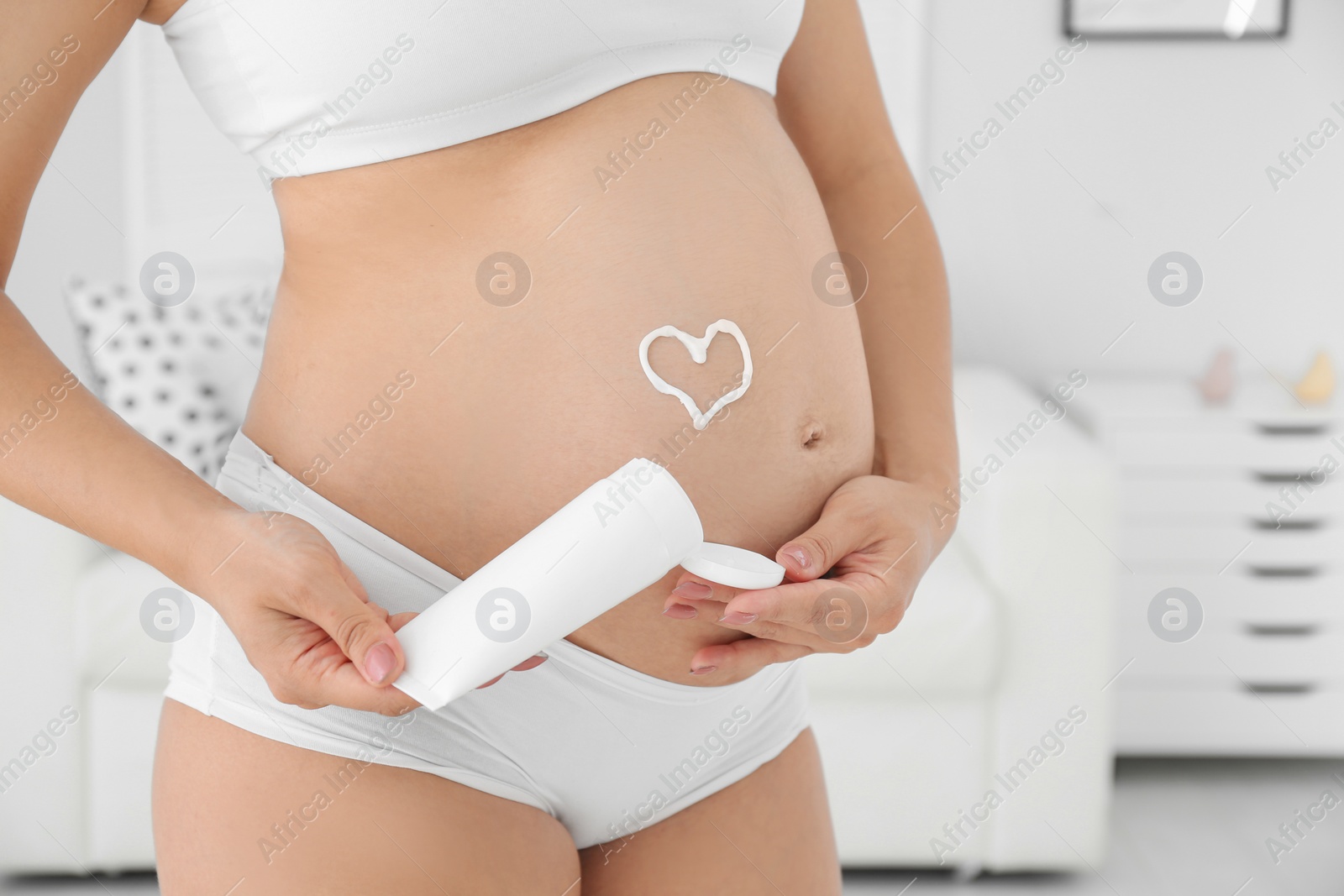 Photo of Heart painted with body cream on pregnant woman's belly at home, closeup