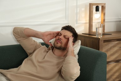 Photo of Man suffering from terrible migraine on sofa at home