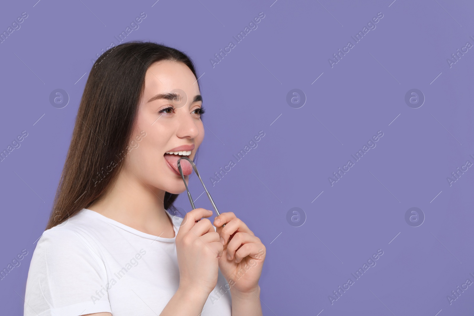 Photo of Happy woman brushing her tongue with cleaner on violet background, space for text