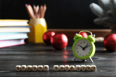 Photo of Cubes with phrase Winter Holidays on black wooden table in classroom. Space for text