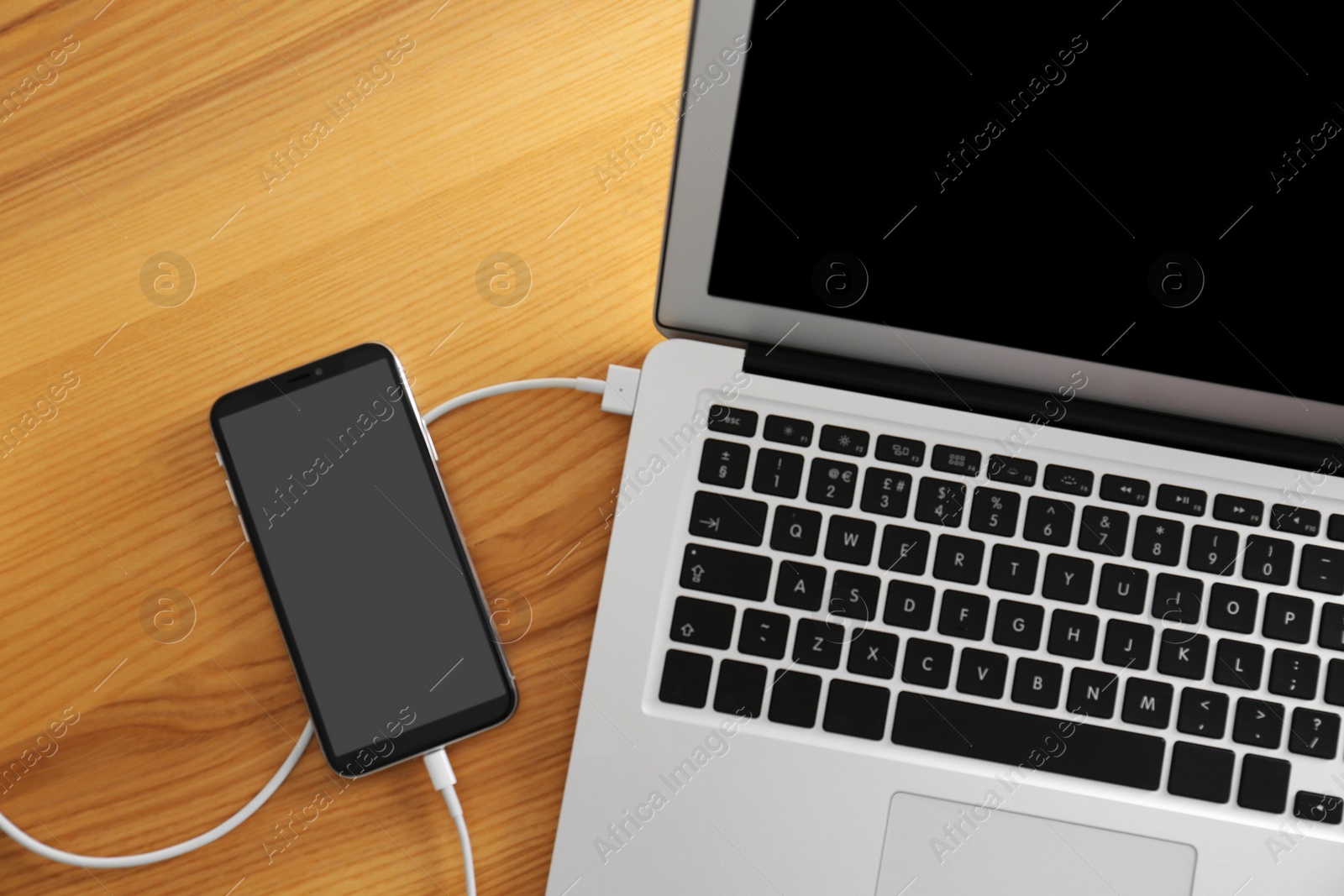 Photo of Modern smartphone charging from laptop on wooden table, top view