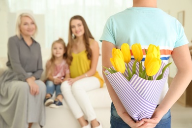 Photo of Little boy hiding tulip bouquet for family behind his back at home