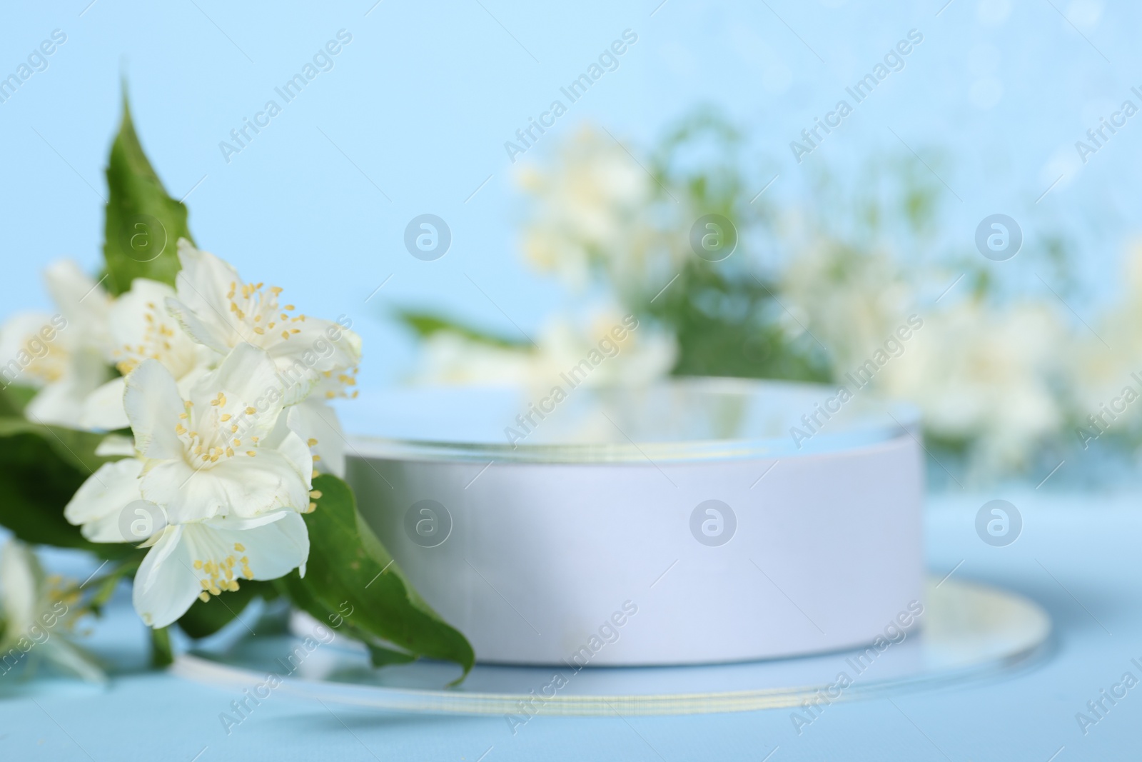 Photo of Presentation of product. White podium and beautiful jasmine flowers on light blue background closeup