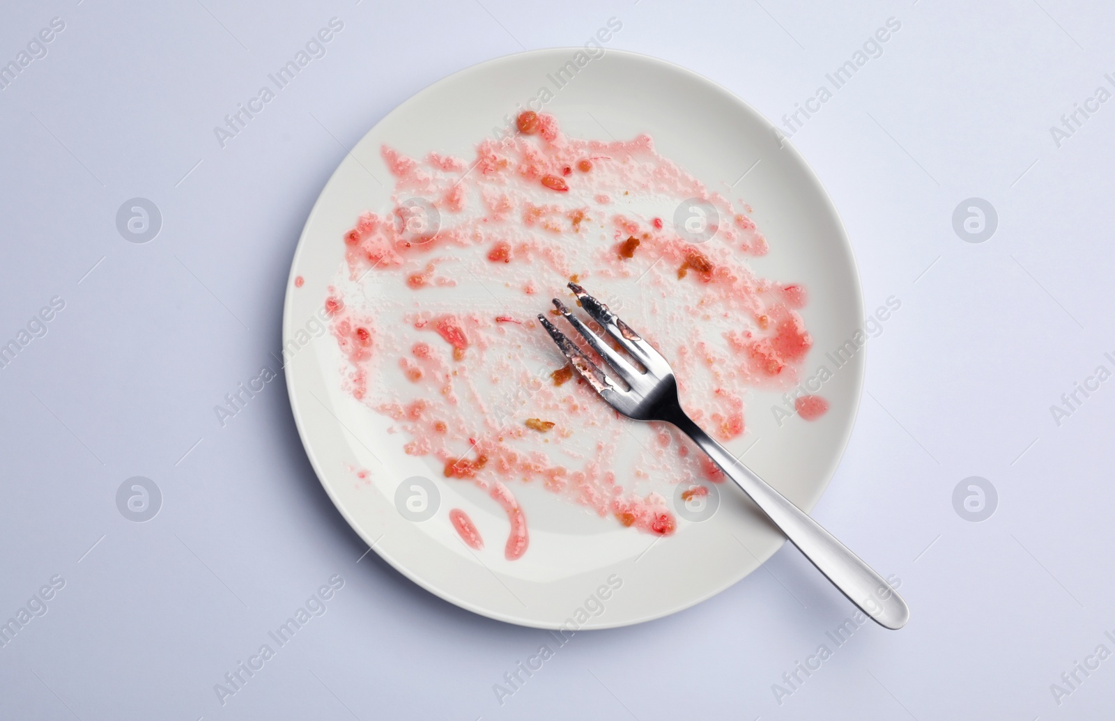 Photo of Dirty plate with food leftovers and fork on white background, top view