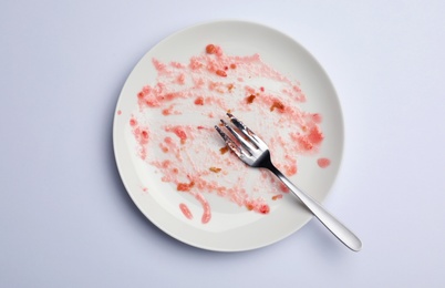 Photo of Dirty plate with food leftovers and fork on white background, top view