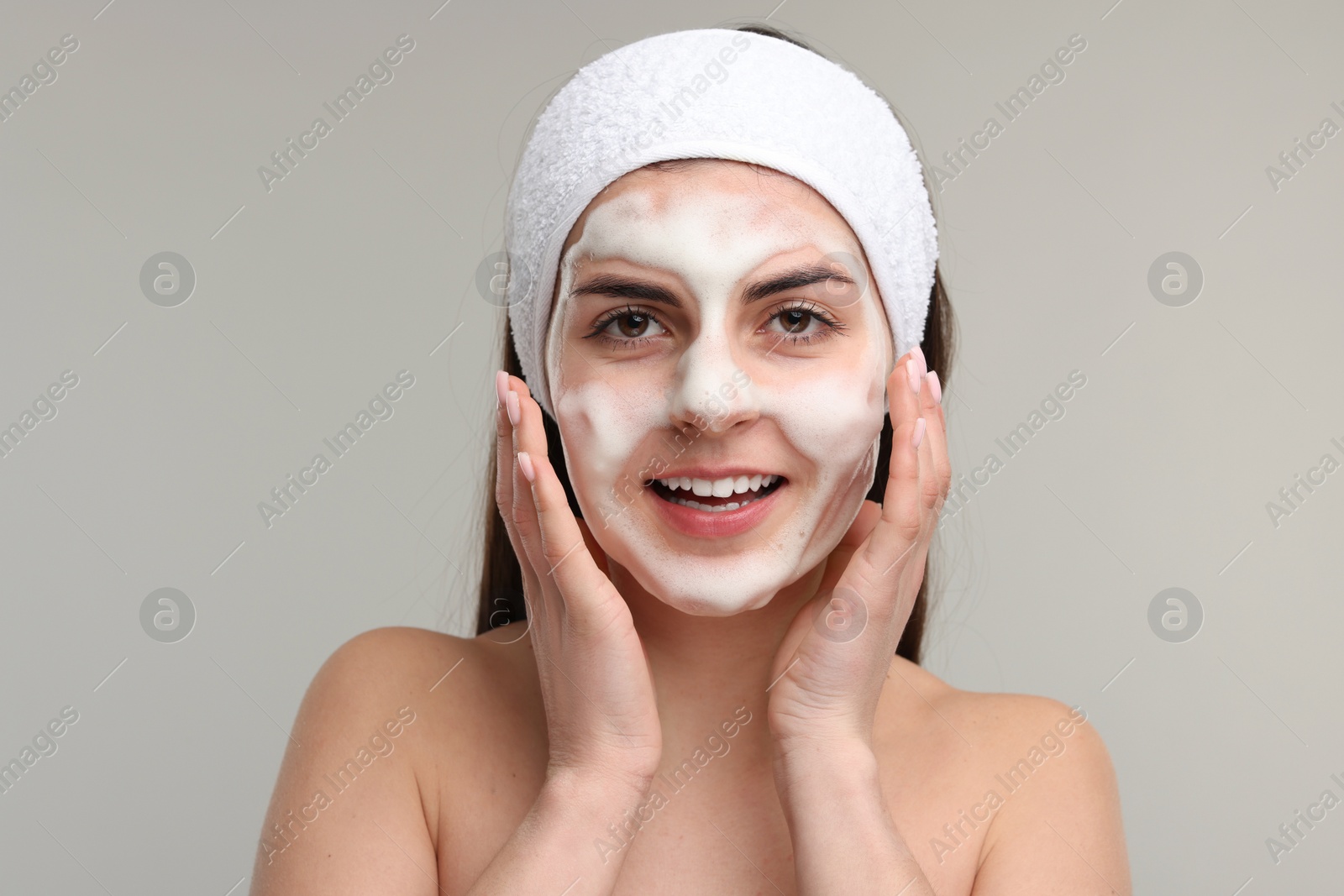 Photo of Young woman with headband washing her face on light grey background