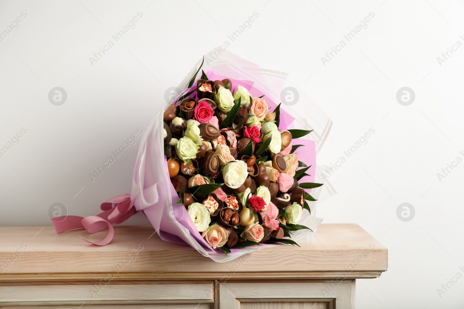 Photo of Beautiful bouquet of flowers and chocolate candies on wooden shelf against white background